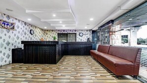 Un espace d’accueil avec un mur à motifs, un comptoir de réception, un canapé marron et un sol à carreaux.