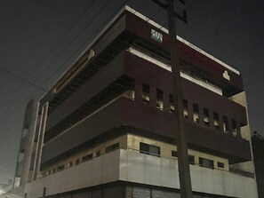 Un edificio de varios pisos con techo plano, grandes ventanales en los pisos superiores y una señal visible en la fachada.
