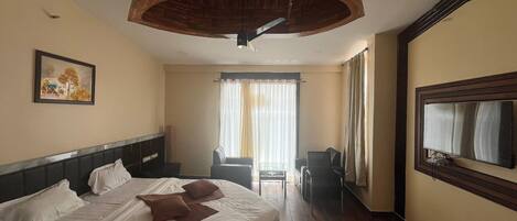 A hotel room with a bed, a desk, a chair, a large mirror, and a ceiling fan.