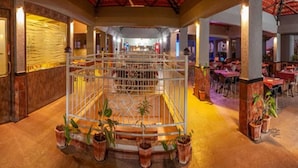 Un vaste espace intérieur doté d’un espace central ouvert, entouré de tables et de chaises, de plantes en pot et d’un plafond remarquable aux carreaux rouges.