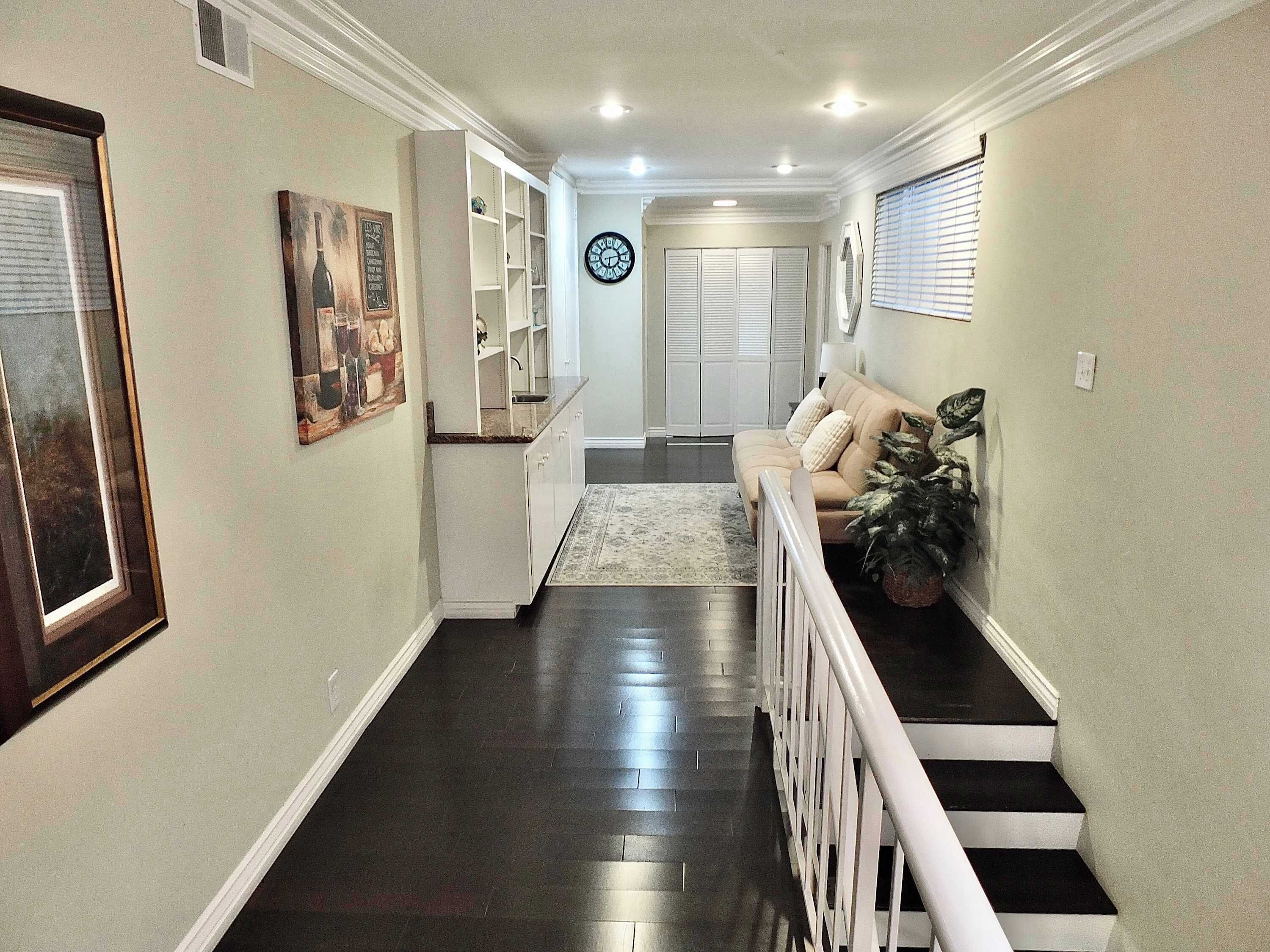 A hallway with a staircase, a sofa, and a clock on the wall.