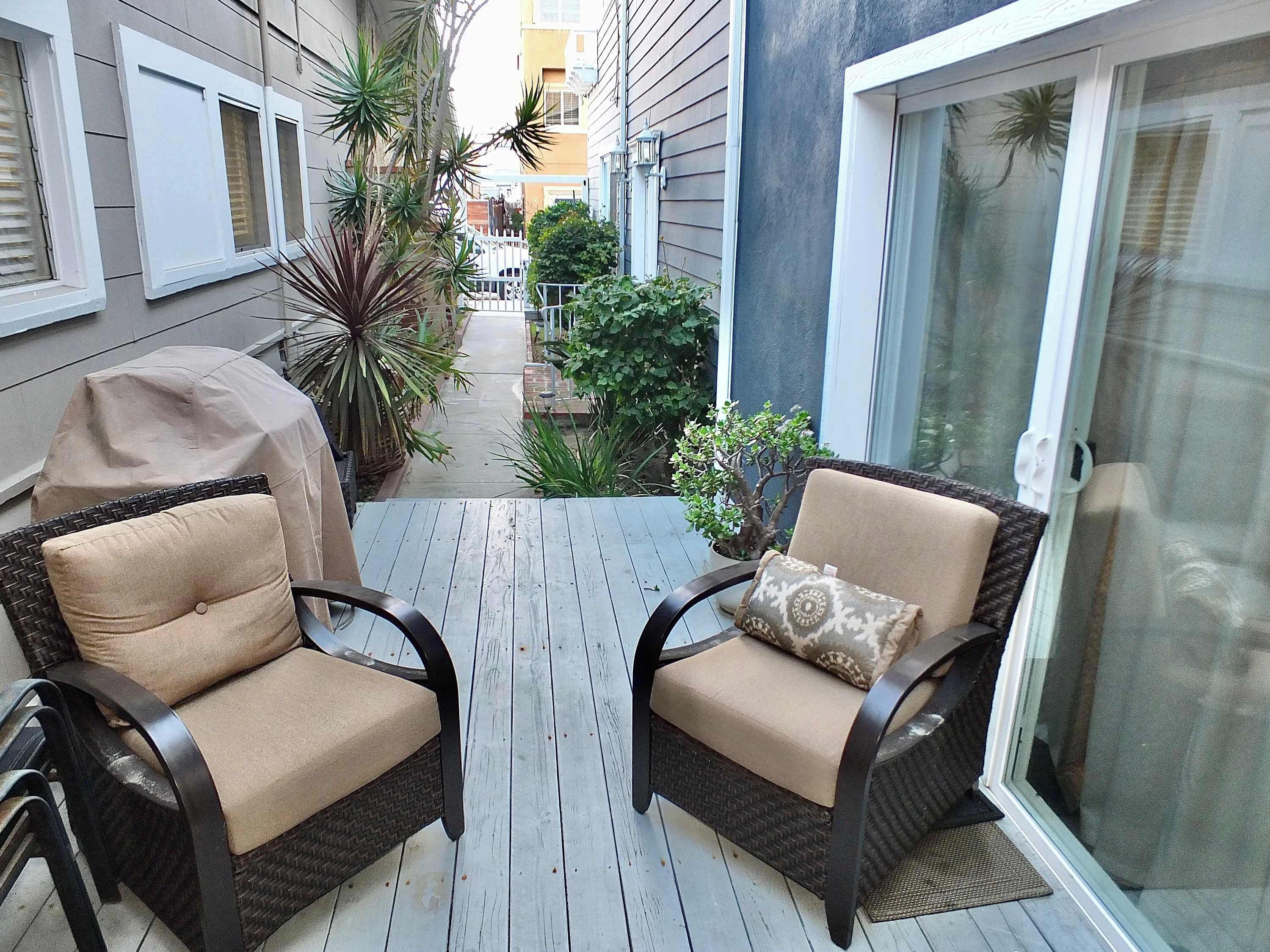 A balcony with two wicker chairs, a small potted plant, and a grill.