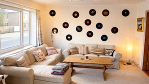 A living room with a sofa, a coffee table, and a wall decorated with vinyl records. - Struer Family House | 600m to Beach, Garden with Trampoline & Play Area (Struer)