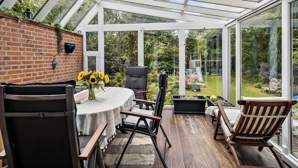 A conservatory with a brick wall, a table with chairs, and a garden view. - Struer Family House | 600m to Beach, Garden with Trampoline & Play Area (Struer)