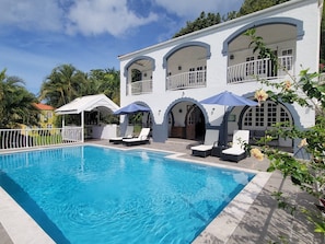 A swimming pool with lounge chairs and umbrellas, surrounded by a white building with arched balconies.