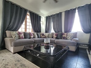 Una sala de estar con un sofá modular, una mesa de centro de vidrio y un tapete estampado.