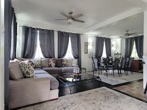 A living room with a sofa, coffee table, dining area with chairs, and ceiling fans.