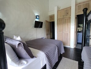 Un dormitorio con una cama, televisión montada en la pared, armarios de madera y un baño visible a través de una puerta abierta.