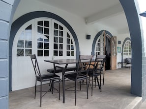A covered patio with a table and chairs, surrounded by white doors with arched tops.