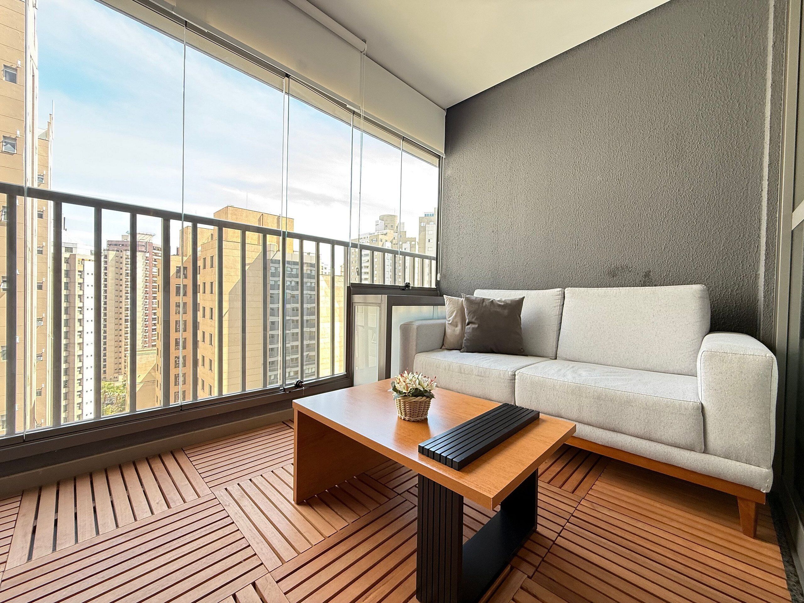A modern living room with a sofa, a wooden coffee table, and a city view through large windows.