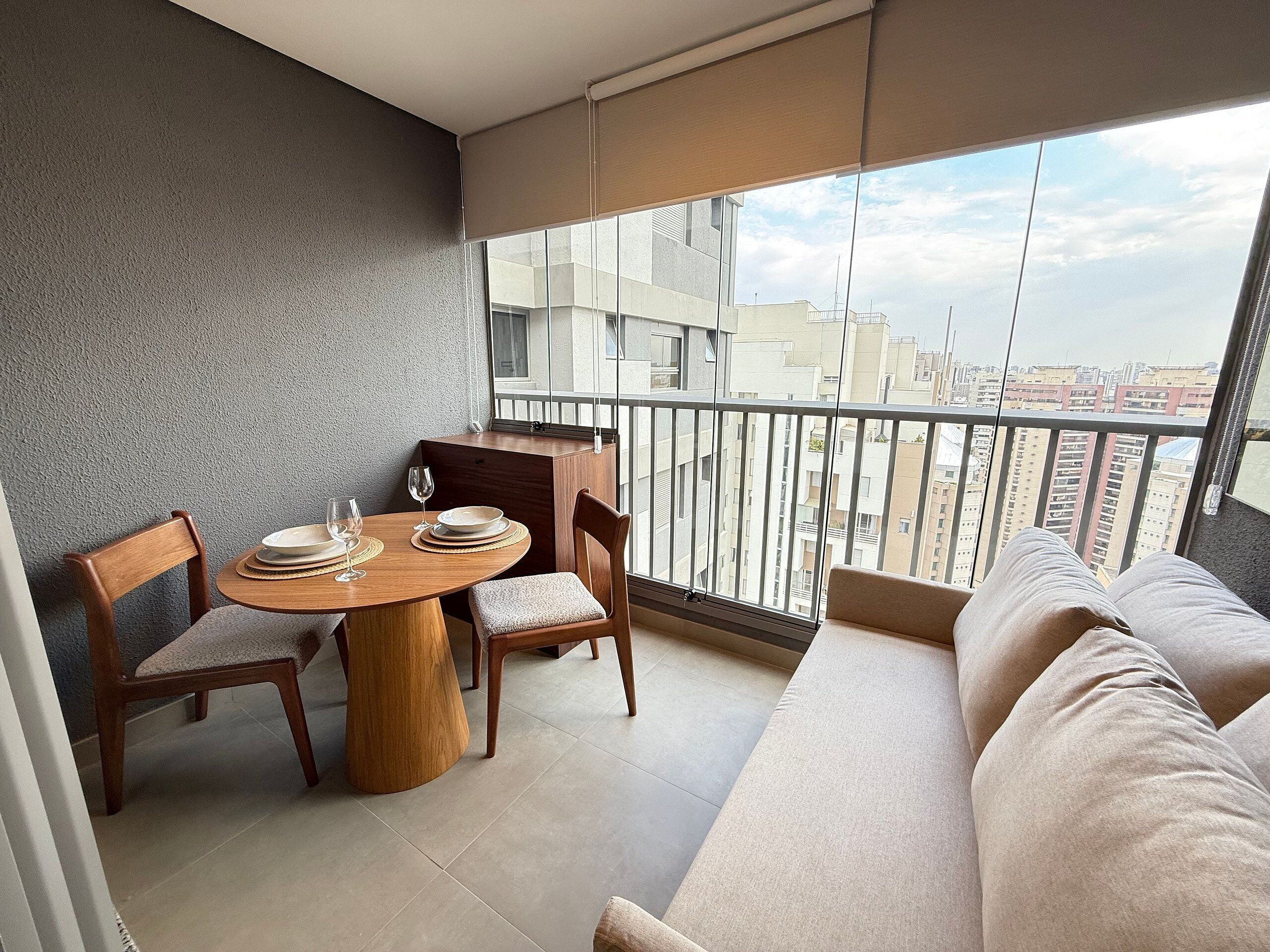 A balcony with a dining table set for four, a sofa, and a view of the cityscape.