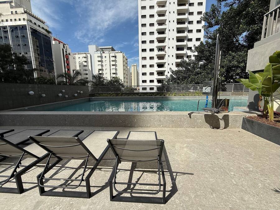 Une piscine entourée de chaises longues, avec de grands immeubles et de la verdure tout autour.