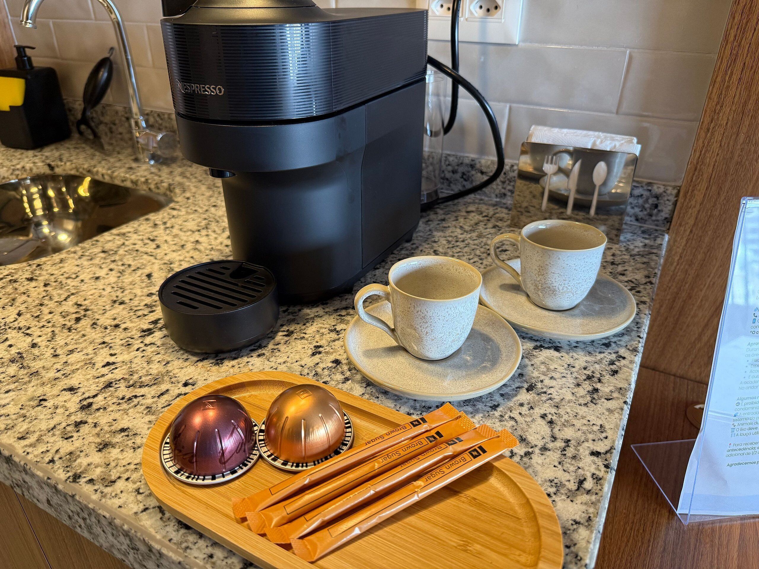Un bancone cucina con una macchina da caffè, due tazze, un vassoio con un misurino e un cucchiaino, e un menu.