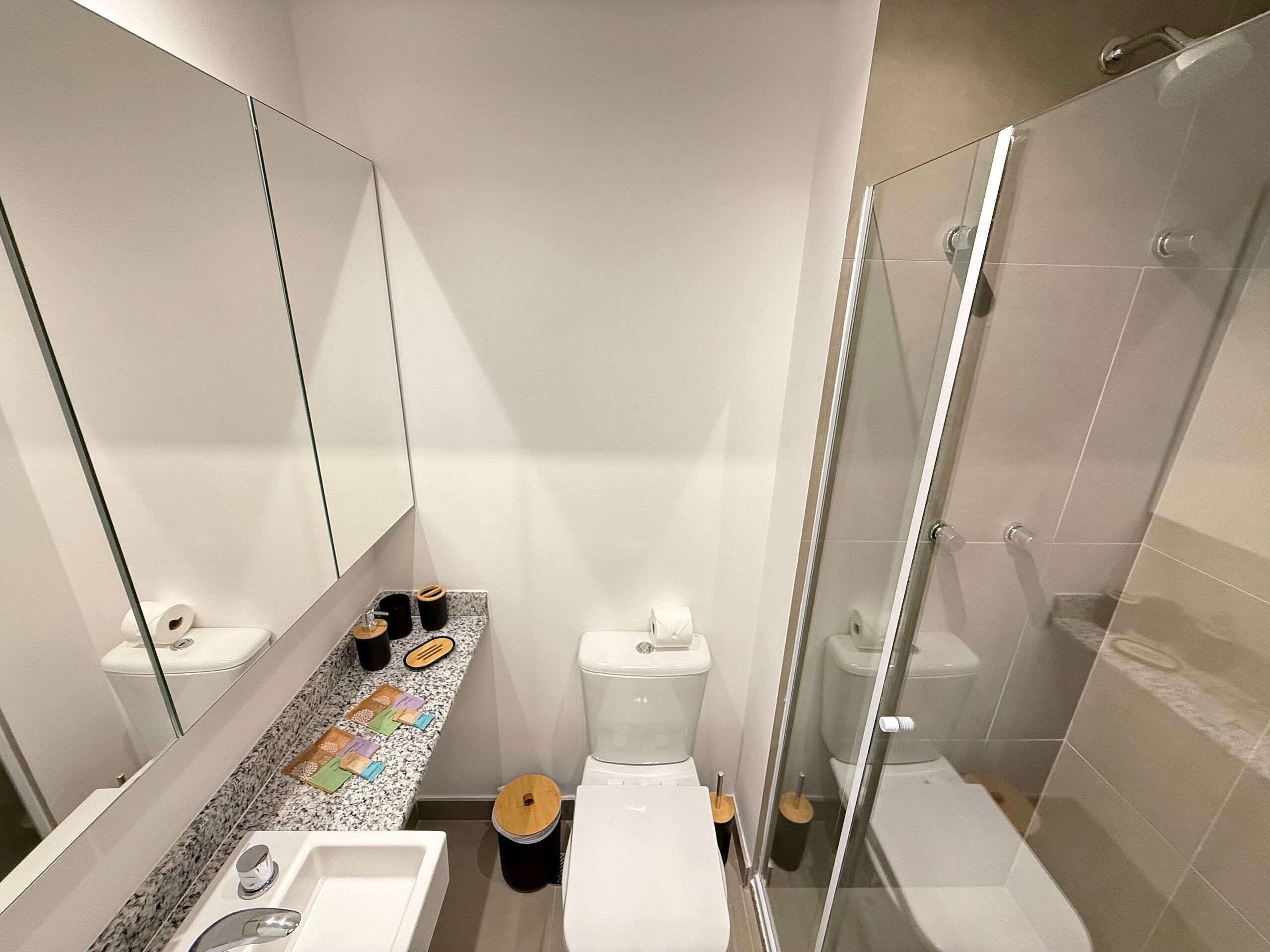 Un baño moderno con cabina de ducha de vidrio, un lavamanos y dos inodoros.