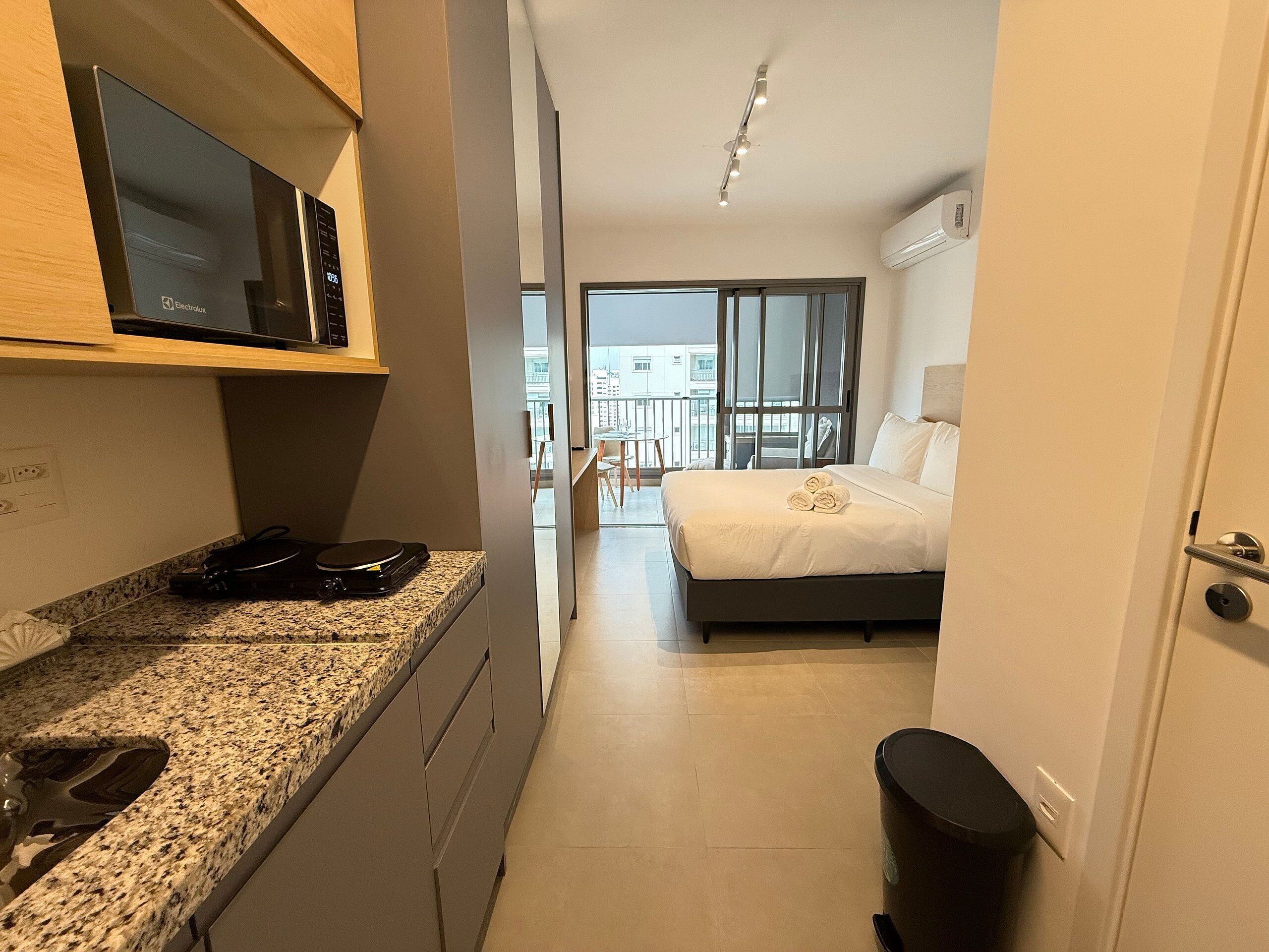 Une chambre d’hôtel équipée d’un lit, d’une télévision, d’un bureau avec un ordinateur et offrant une vue sur la ville grâce à de grandes fenêtres.