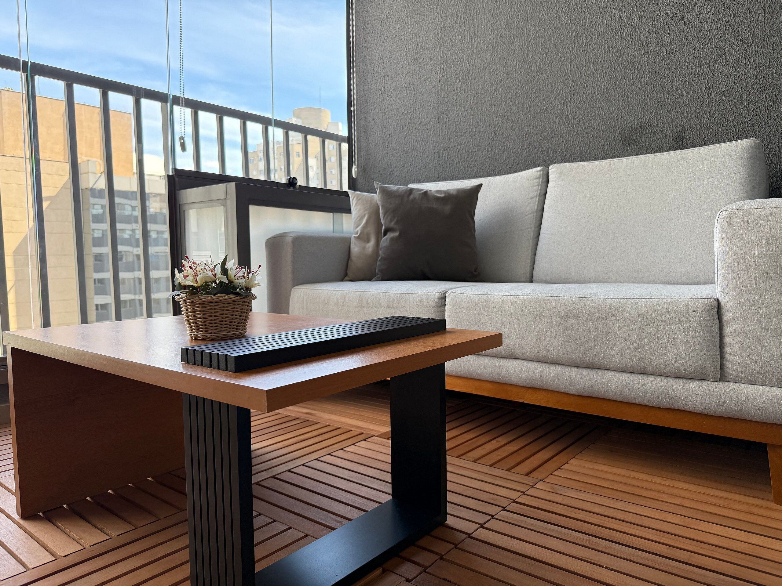 Een moderne woonkamer met een grijze bank, een houten salontafel met een toetsenbord, en een rieten mand met bloemen.