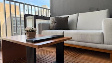 Ein modernes Wohnzimmer mit einem grauen Sofa, einem Holztisch mit Tastatur und einem Korbwägelchen mit Blumen.