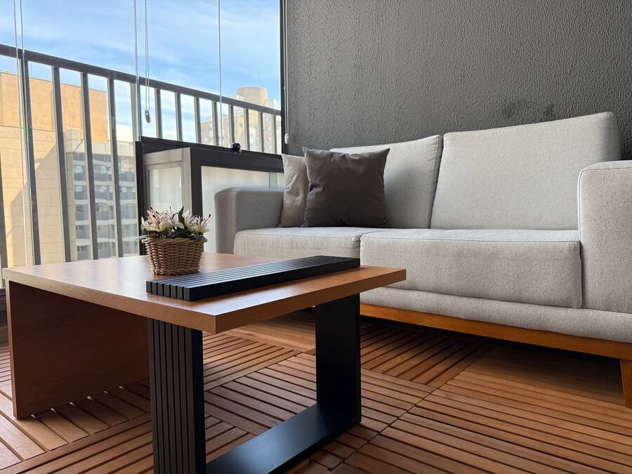 Ein modernes Wohnzimmer mit einem grauen Sofa, einem Holztisch mit Tastatur und einem Korbwägelchen mit Blumen.