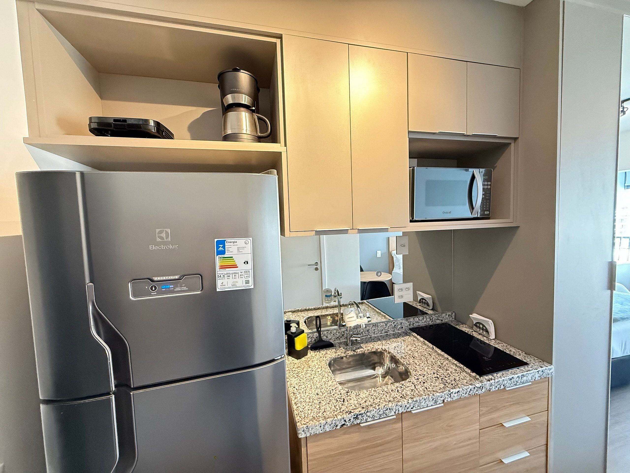 A compact kitchen with a stainless steel refrigerator, a microwave, and a coffee maker on the countertop.