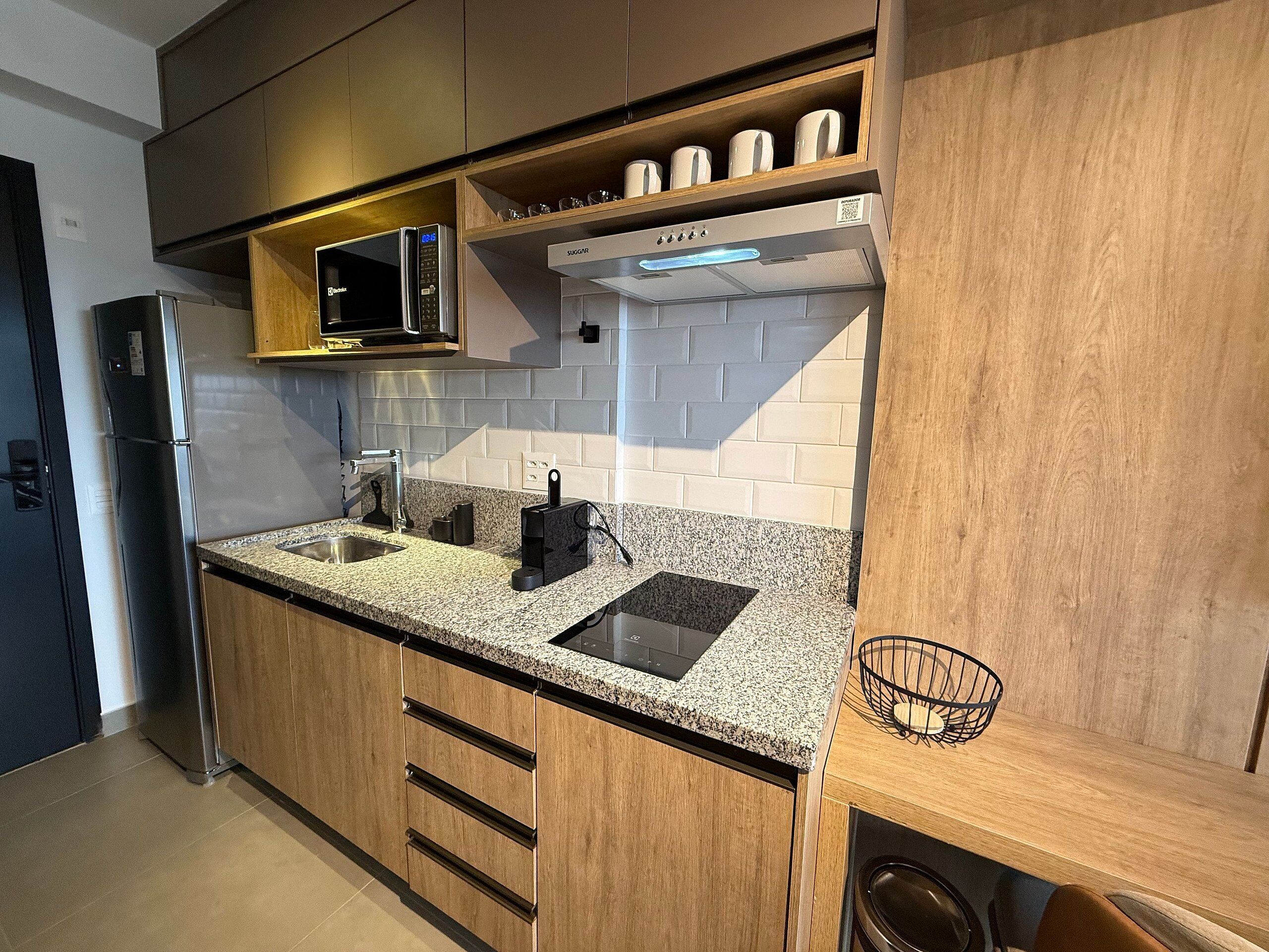 A modern kitchen with granite countertops, stainless steel appliances, wooden cabinets, and a microwave above the sink.