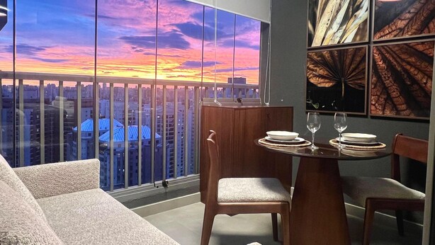 A modern dining area with a city view, a table with plates and glasses, and a sofa. - Livinn - On Jurupis (São Paulo)