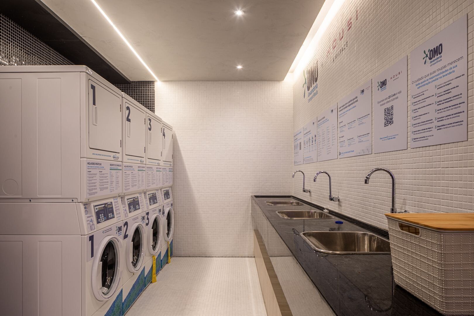 A laundry facility with multiple washing machines, sinks, and informational posters on the wall.