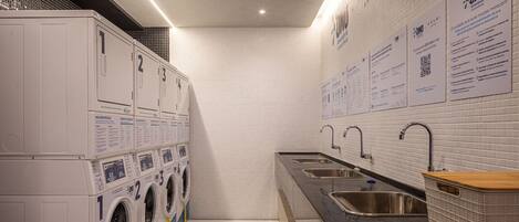 A laundry facility with multiple washing machines, sinks, and informational posters on the wall.