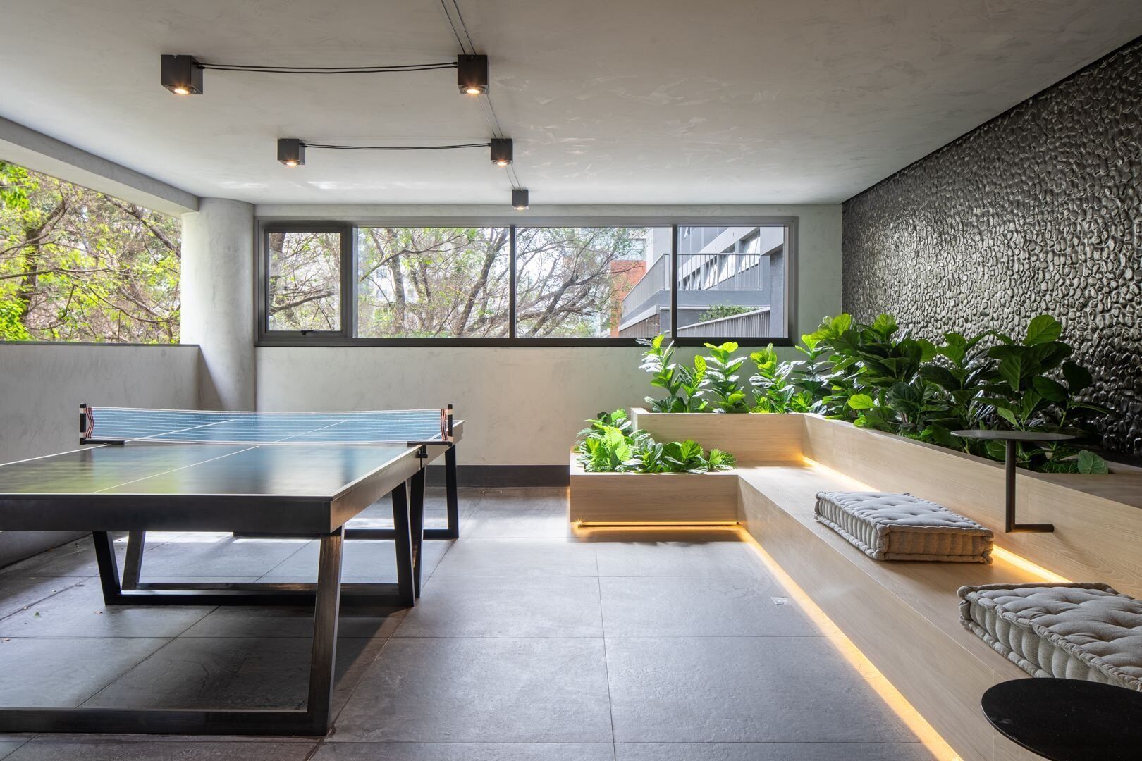 Un espacio interior moderno con mesa de ping pong, zona de estar con cojines y una pared con textura.