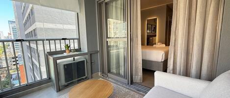 A modern hotel room with a balcony, a round wooden coffee table, a sofa, and a bed with curtains.