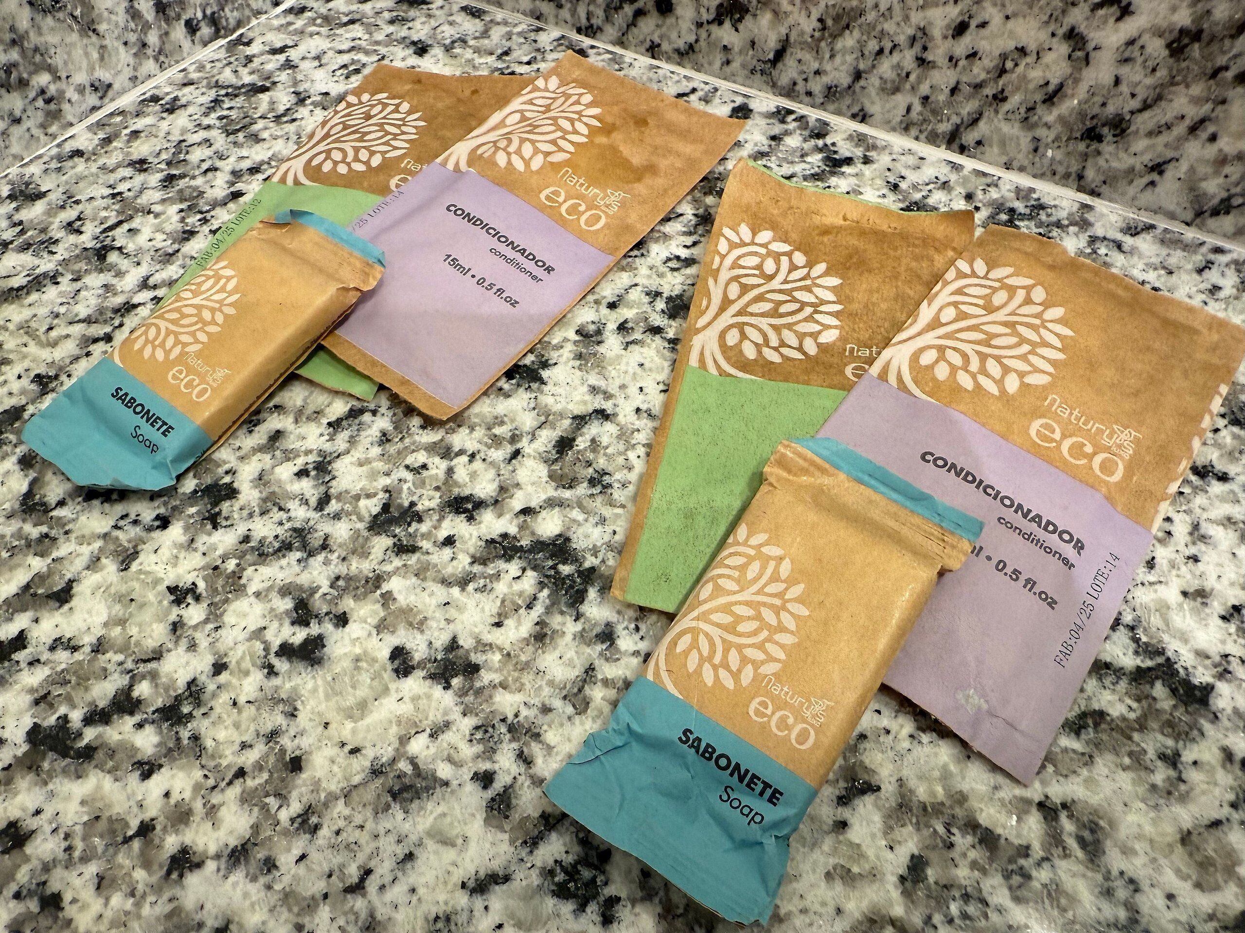 Fire brune papirsposer med 'naturals eco'-branding, hver indeholdende et forskelligt produkt: sæbe, balsam og en anden variant af sæbe.