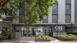 A modern building with a glass entrance, outdoor seating area, and greenery. - Livinn - On Jurupis (São Paulo)