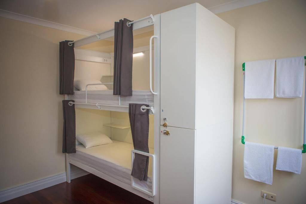 Un lit superposé avec un meuble fixé au mur, un porte-serviettes avec deux serviettes et une prise électrique visible.
