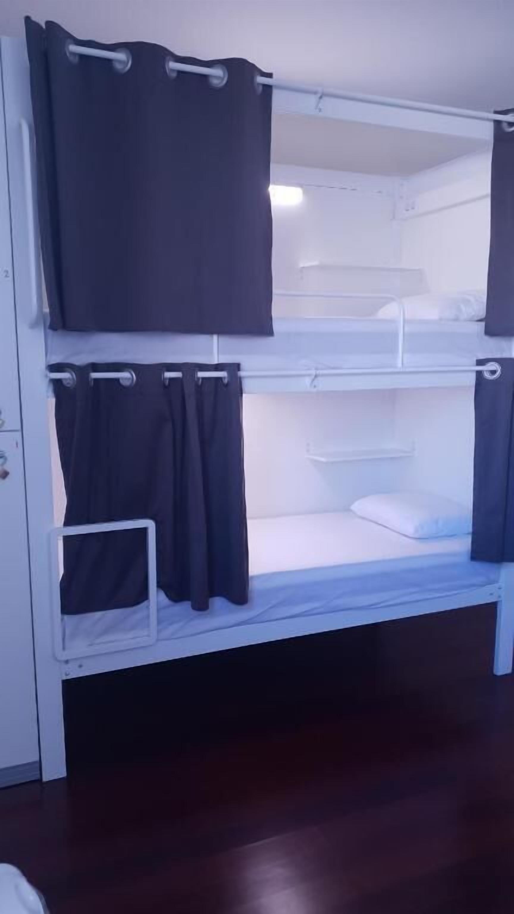 A bunk bed with curtains, a white headboard, and a bedside table.
