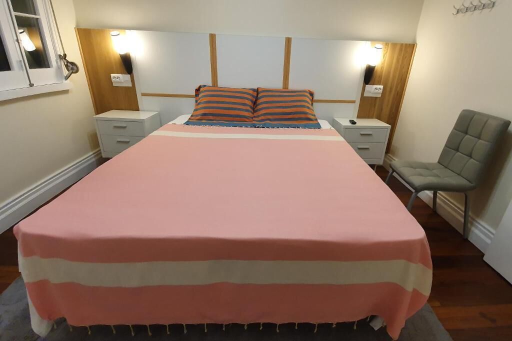 Ein Schlafzimmer mit einem großen Bett, zwei Nachttischen, einem Sessel und einem Kopfteil mit integrierter Beleuchtung.