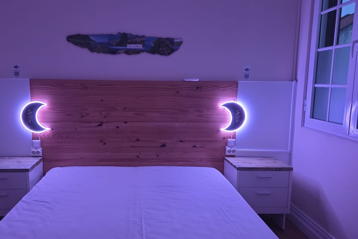 A bedroom with a wooden headboard, two bedside tables, a bed, and a wall-mounted artwork.
