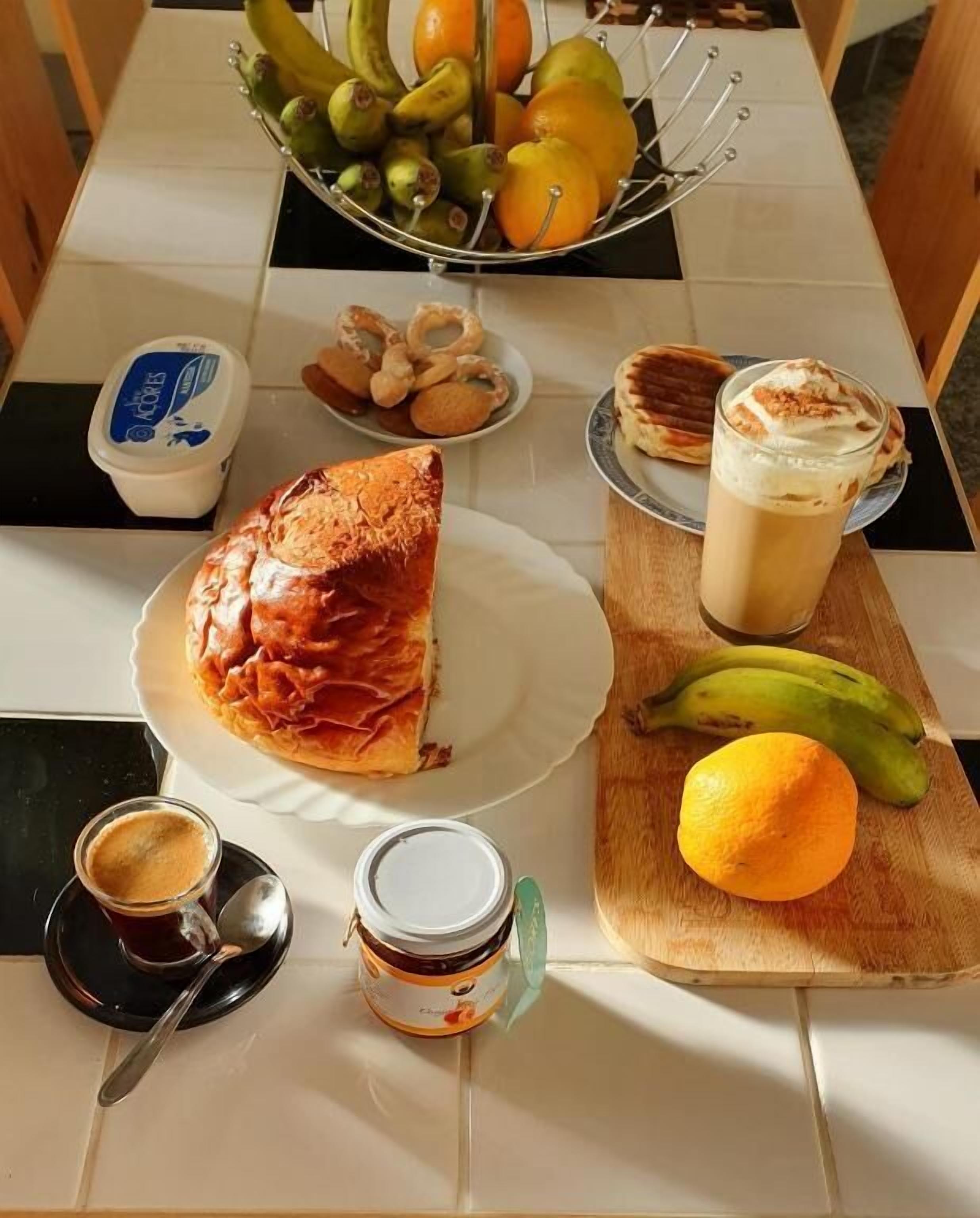 Une table à manger avec une part de pizza, un verre de café glacé, une tasse de café, un bol de fruits et une assiette de biscuits.
