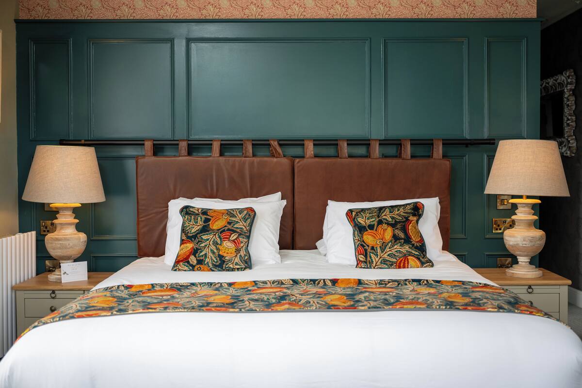 A neatly made bed with a floral bedspread, two decorative pillows, and two bedside lamps on a nightstand.
