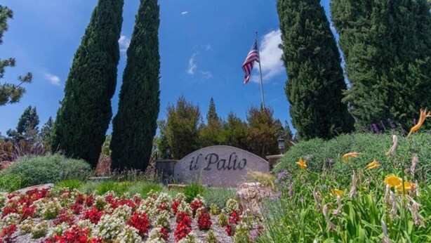 A sign with "il Palazzo" written on it, surrounded by tall cypress trees and colorful flowers. - Cozy Casa | Executive Condo•Pool•Spa•Sauna•BBQ (San Diego)