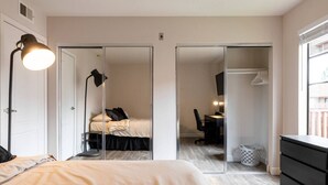 A bedroom with a bed, bedside lamp, and a desk with a chair. There is a closet with sliding doors and a window with blinds. - Cozy Casa | Executive Condo•Pool•Spa•Sauna•BBQ (San Diego)