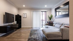 A modern living room with a grey sofa, a flat-screen TV, a black entertainment unit, and a patterned rug. - Cozy Casa | Executive Condo•Pool•Spa•Sauna•BBQ (San Diego)