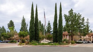 A residential area with tall cypress trees, a flagpole with an American flag, and a sign reading "il Palazzo". - Cozy Casa | Executive Condo•Pool•Spa•Sauna•BBQ (San Diego)