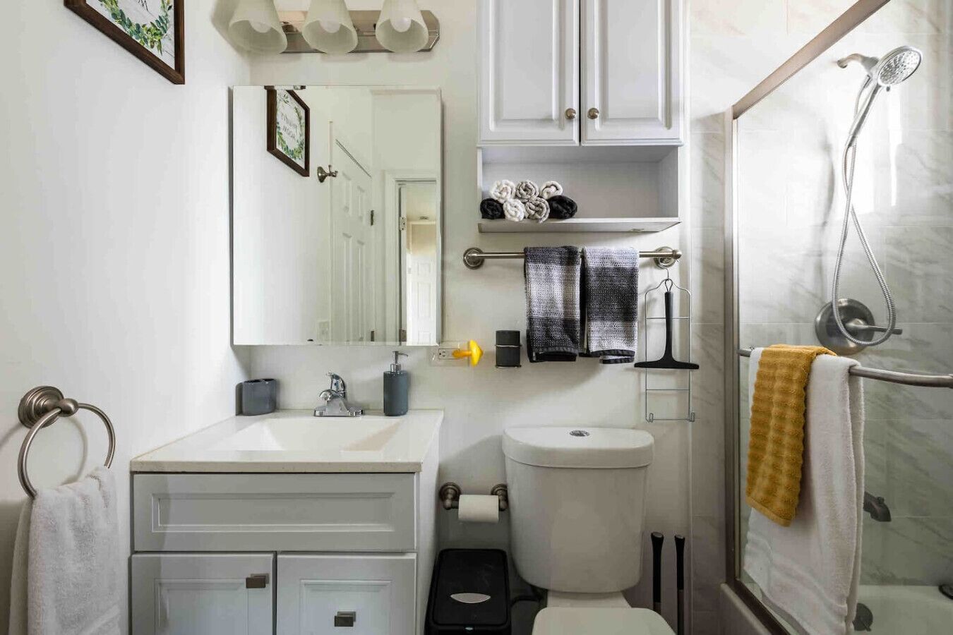A bathroom with a white sink, mirror, toilet, and shower. There are towels and toiletries on shelves.