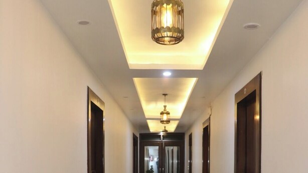 A hallway with a modern ceiling design, potted plants, and a central light fixture. - HOTEL CASA DOON (Dehradun)