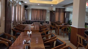 A restaurant with a long wooden dining table, cushioned seating, and pendant lighting. - HOTEL CASA DOON (Dehradun)