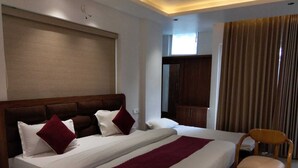 A hotel room with a large bed, a wooden headboard, a wooden chair, a small table, and a wardrobe. - HOTEL CASA DOON (Dehradun)