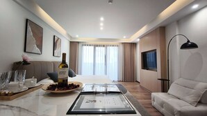 A modern hotel room with a bed, a seating area with a sofa, a dining table with a wine bottle, and a TV mounted on the wall. - Sleek Apartment in the Heart of Piraeus (Piraeus)