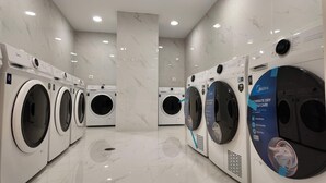 A row of modern, white front-loading washing machines in a well-lit, marble-floored laundry room. - Sleek Apartment in the Heart of Piraeus (Piraeus)