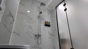 A modern bathroom with a marble shower wall, a handheld showerhead, and a wall-mounted faucet. - Sleek Apartment in the Heart of Piraeus (Piraeus)