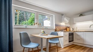 Una cocina moderna con armarios blancos, encimera de madera y zona de comedor con dos sillas azules.