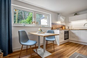 Eine moderne Küche mit weißen Schränken, einer Holz Arbeitsplatte und einem Essbereich mit zwei blauen Stühlen.